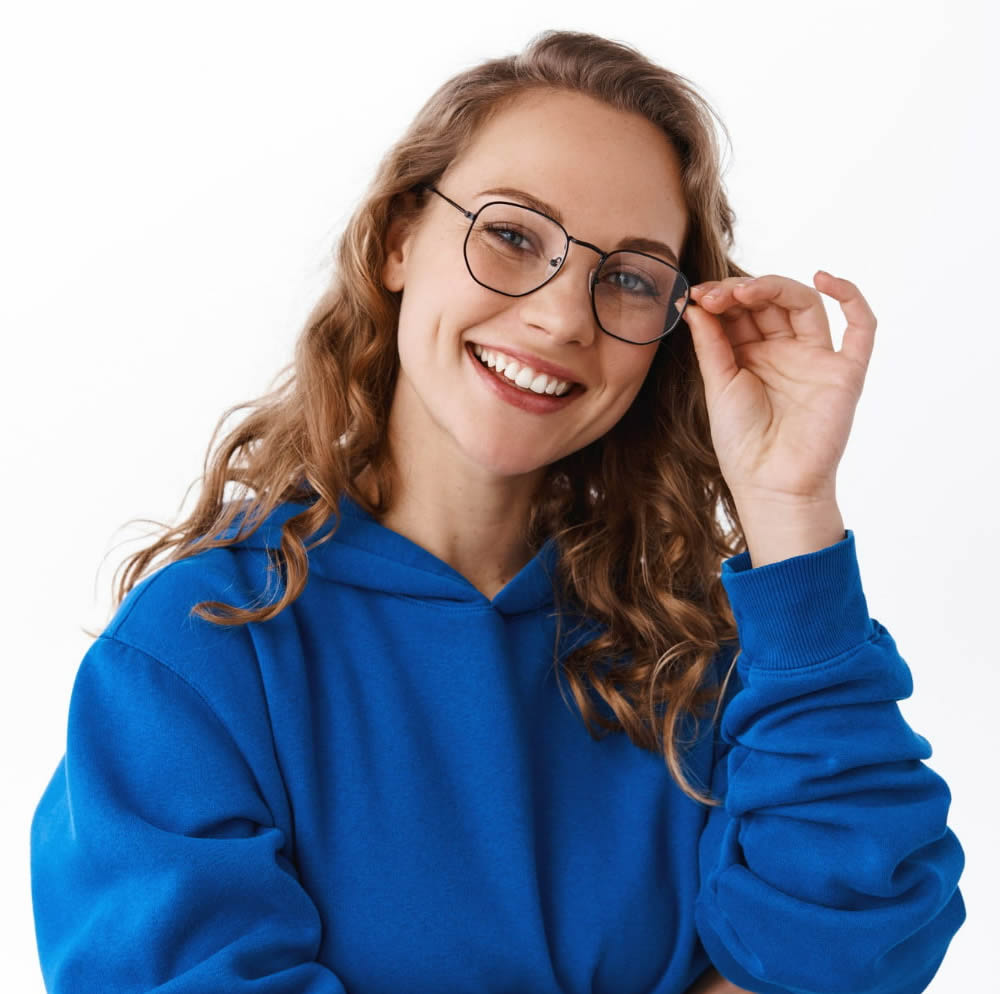 Mulher jovem com roupa azul sorrindo e segurando o óculos no rosto.
